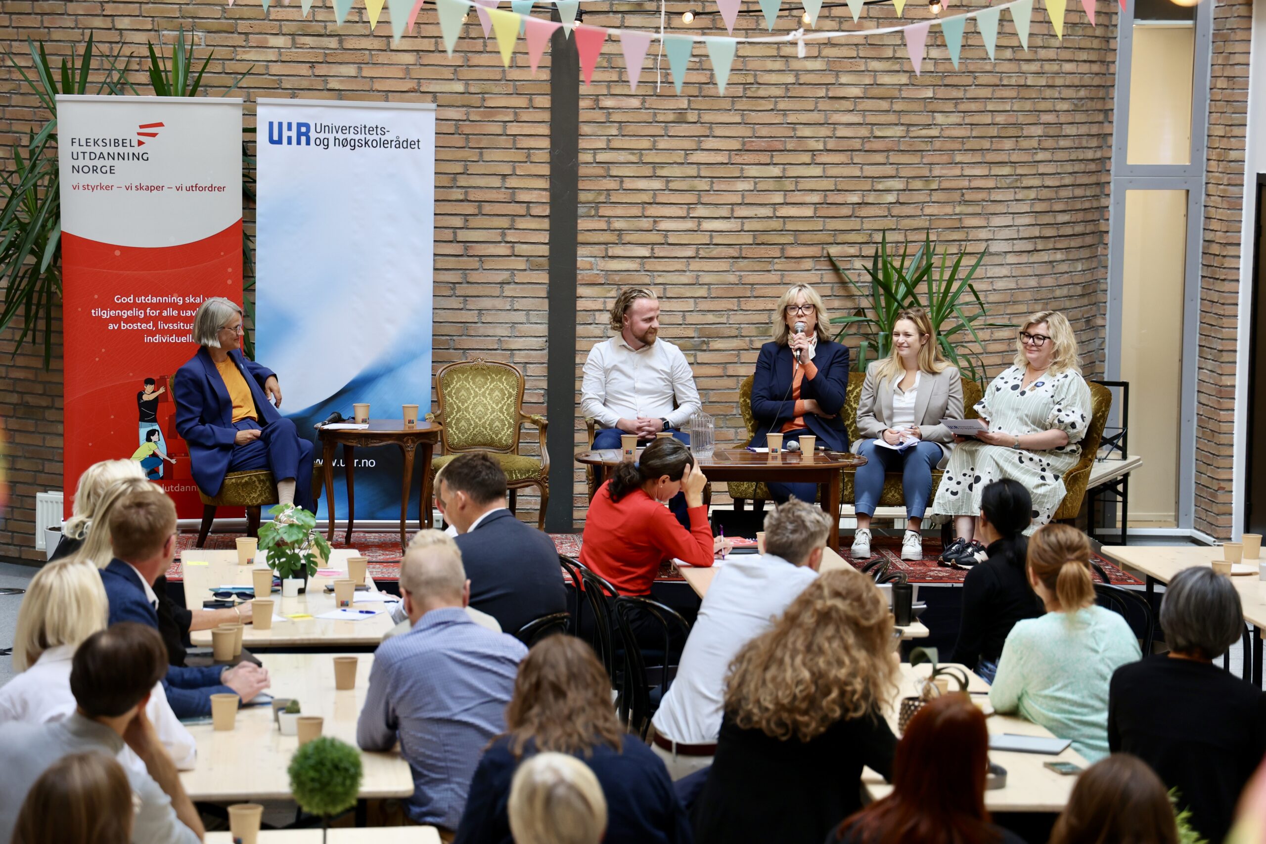Bilder fra en paneldebatt på en scene med ordstyrer og fire paneldeltakere