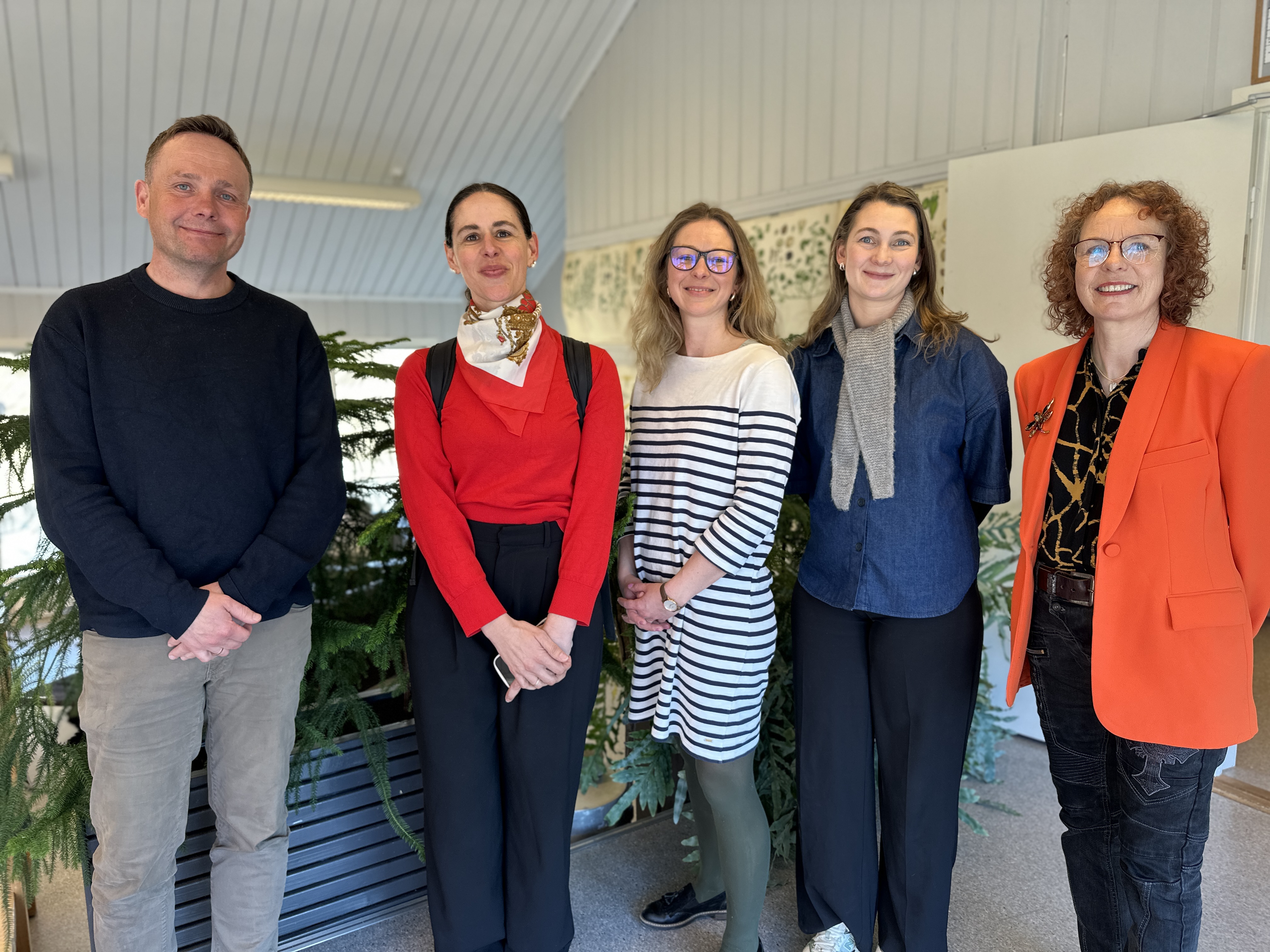 Gruppebilde av fem oppstilte voksne personer innendørs.